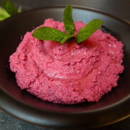 pink beetroot hummus with peppermint leaves in a black bowl